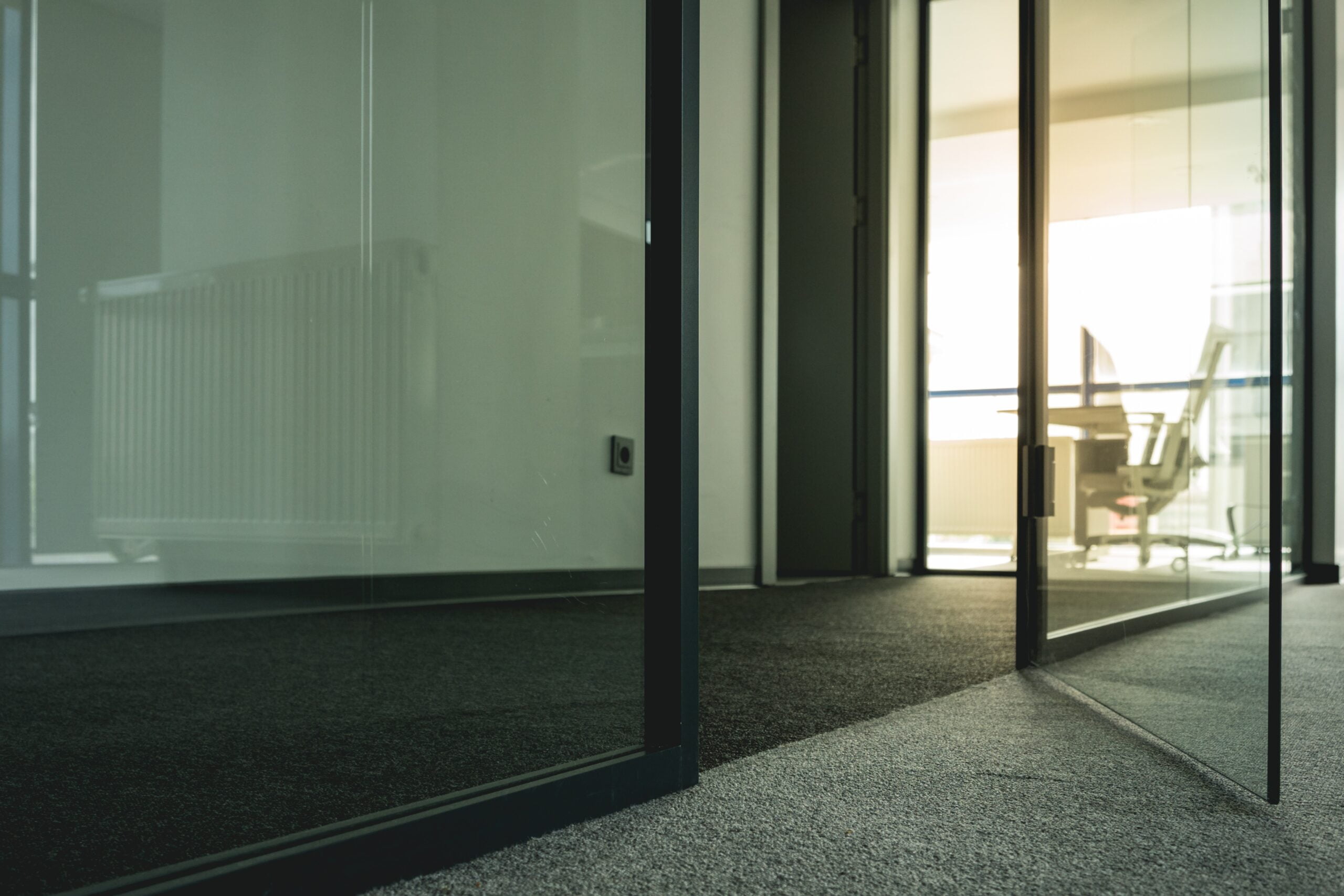Inside an office building, Dark grey carpet with glass walls and door more than half way opened